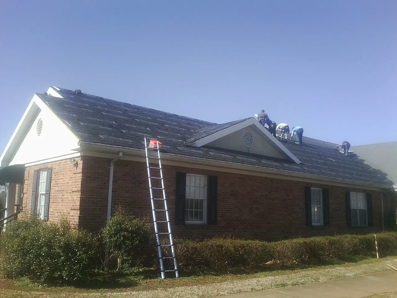 Crew tearing shingles off a brick ranch roof with a ladder set — Metal Roof Repair work by our crew in Uxbridge