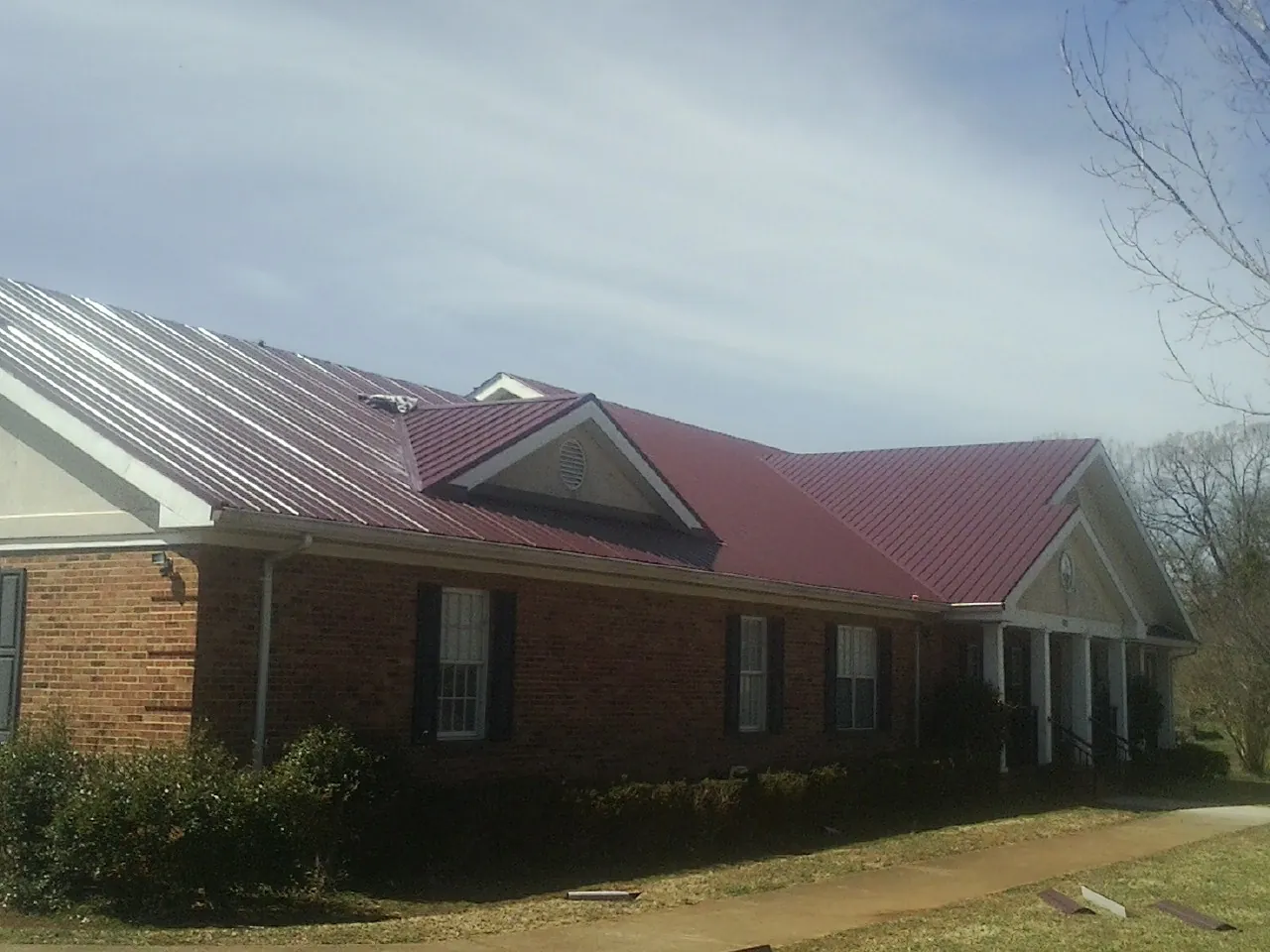 Red metal roof with gabled entries on a long brick building, from a Hail Damage Roof Repair job in Uxbridge