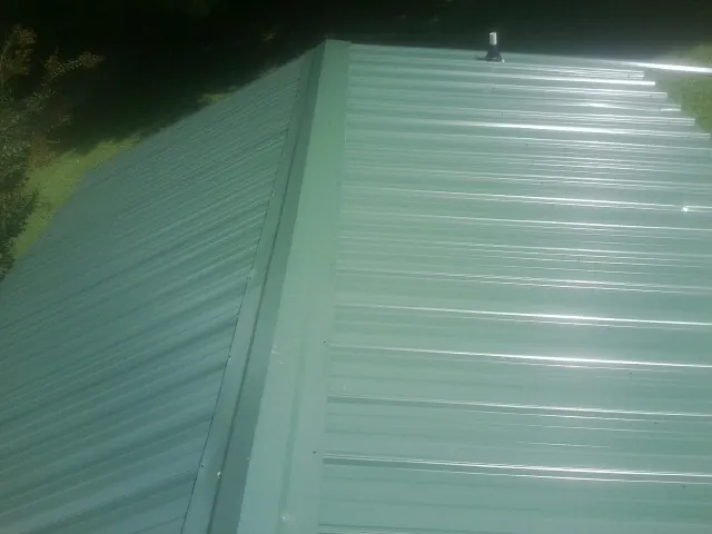 New green metal panels meeting at the ridge of a roof — Flat Roof Repair work by our crew in Uxbridge