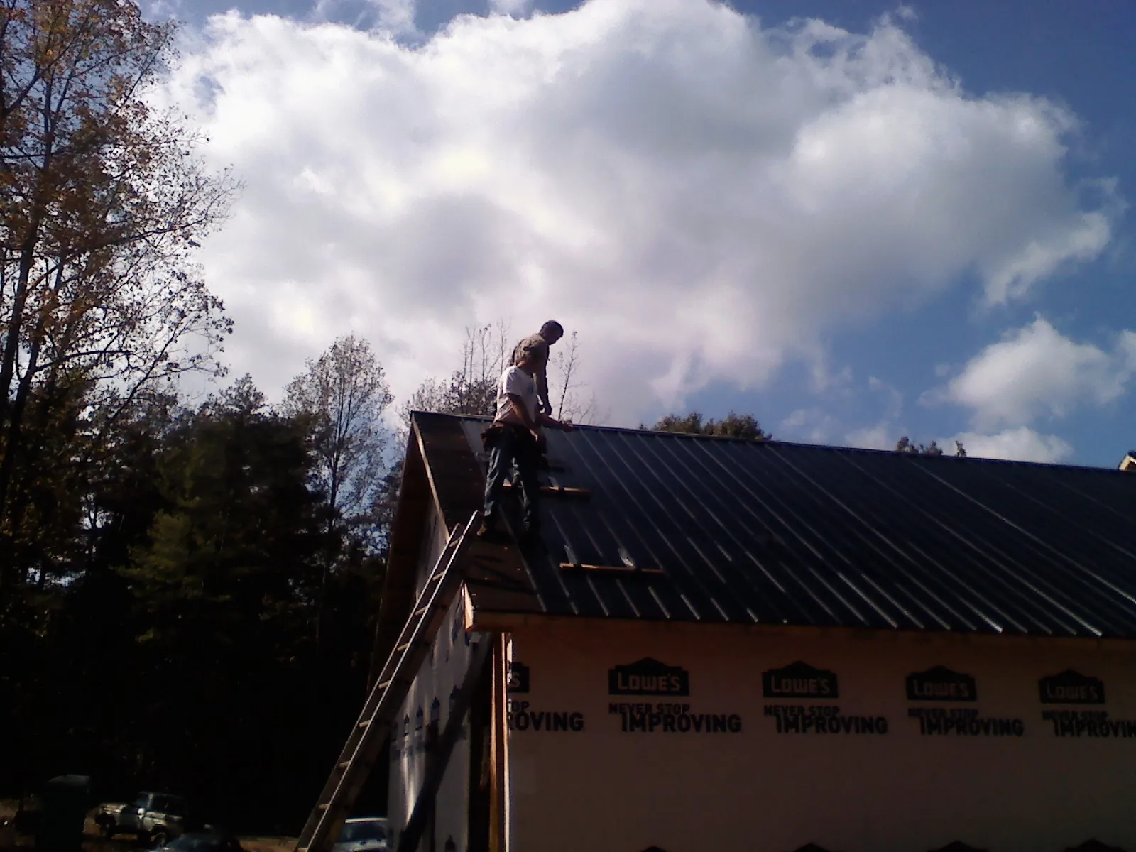 Roofer fastening dark metal panels high against a cloudy sky, from a Roof Inspection job in Uxbridge