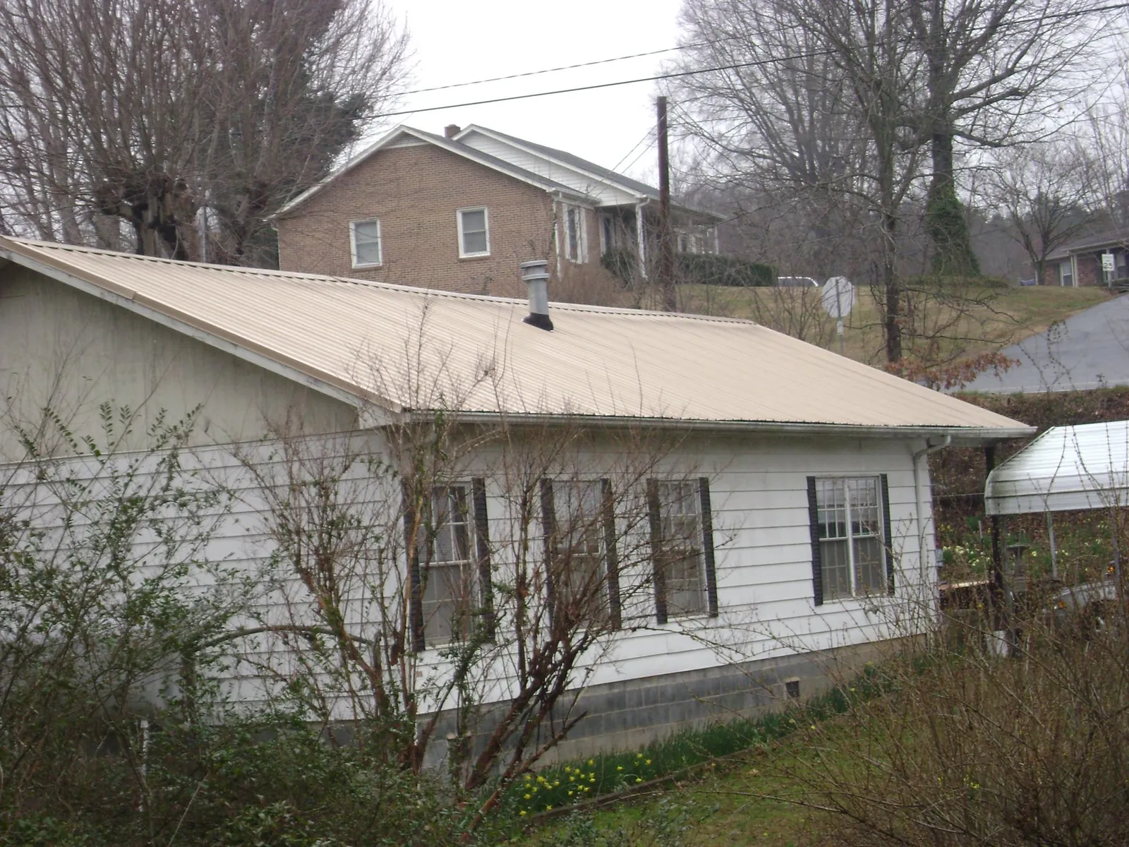 Tan metal roof on a white sided house set into a hillside — Commercial Roofing by Roofing Brothers in Uxbridge